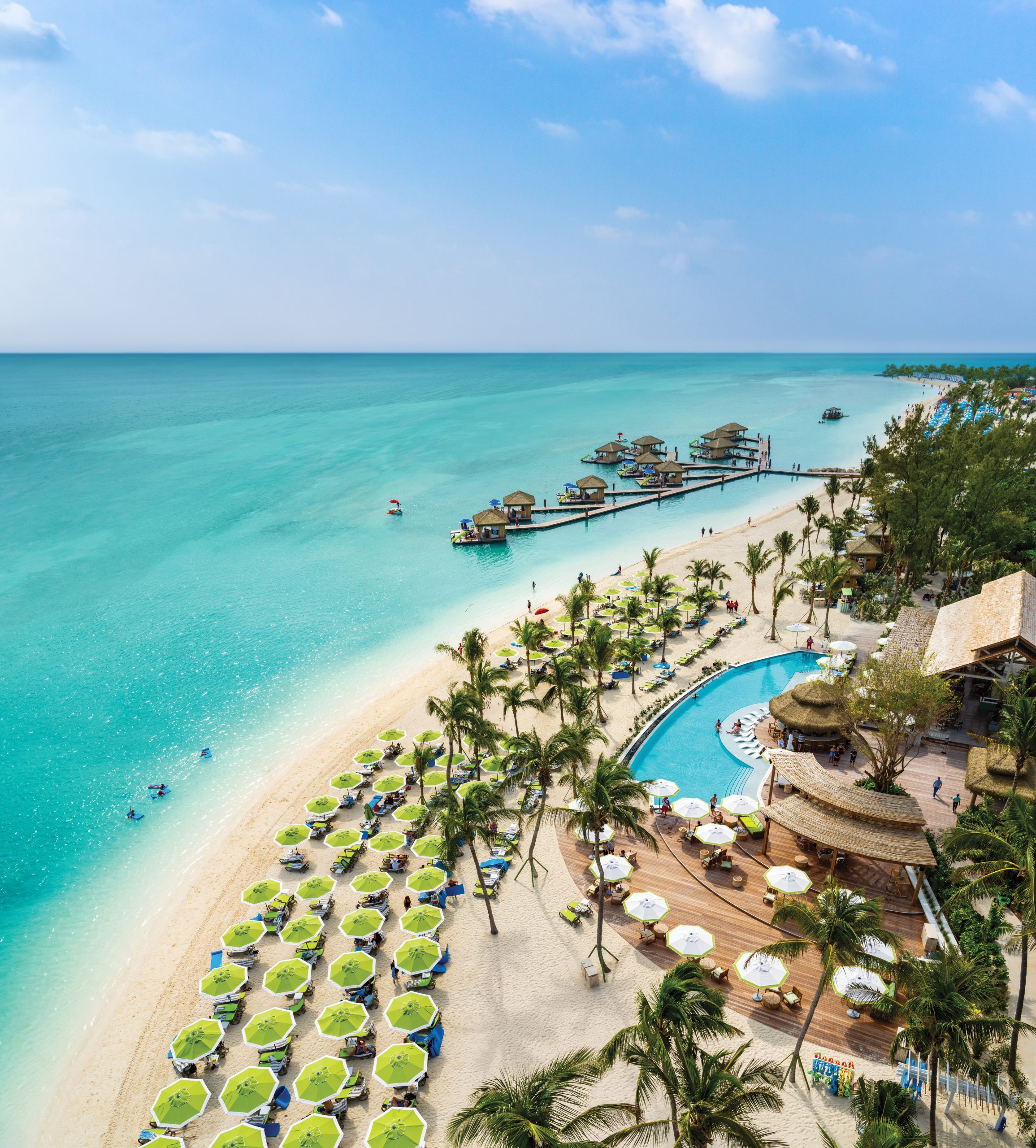 Perfect Day at CocoCay, Coco Beach Club,  high drone shot of beach showing shoreline, Floating Cabanas, sandy beach, green beach umbrellas and lounge chairs, bar, Infinity Pool, and Clubhouse